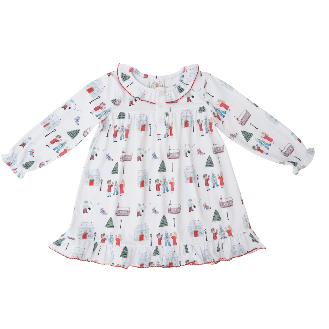A long-sleeve baby dress with a white base and an all-over winter holiday print featuring snowmen, Christmas trees, sleighs, and snow globes. The dress has a ruffled collar and a ruffled hem with red piping, shown flat on a white background.