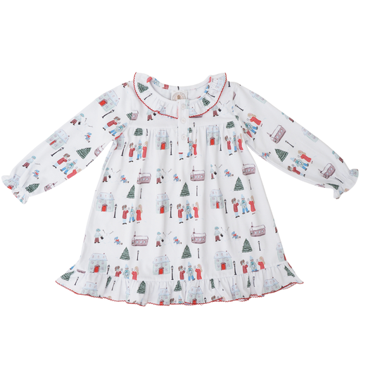 A long-sleeve baby dress with a white base and an all-over winter holiday print featuring snowmen, Christmas trees, sleighs, and snow globes. The dress has a ruffled collar and a ruffled hem with red piping, shown flat on a white background.