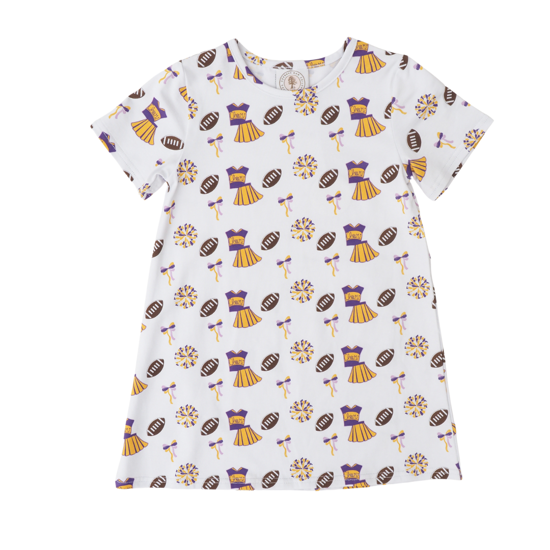 A white short-sleeve play dress with an all-over print of purple and gold cheerleaders, footballs, and pom-poms, displayed flat against a white background.